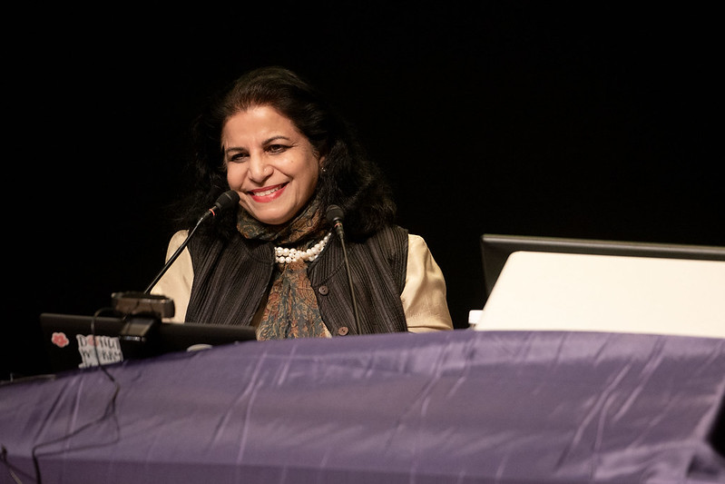 Nandini Tandon smiles and leans to the right. She stands behind a podium, mid-speech.