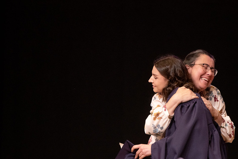 Faith Donithan and Professor Ellis hug. Faith wears purple graduation regalia, while Professor Ellis wears a white floral blouse.