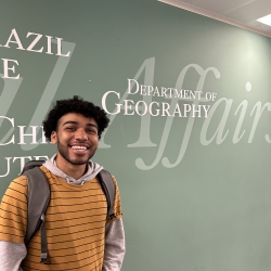 Lee in front of a green wall saying Department of Geography